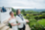 Bride and groom laugh joyfully as they open champagne, at Tiffanys Maleny surrounded by lush greenery and distant mountains under a cloudy sky.