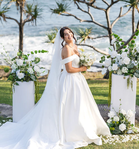 Beautiful bride in full white dress smiling as she stands in front of gorgeous romantic and classic green and white styling at her wedding ceremony