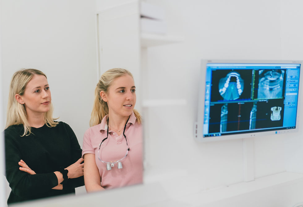 Blond female patient left and blond female dentist with pink pollo shirt are both looking confidently at an x-ray screen.