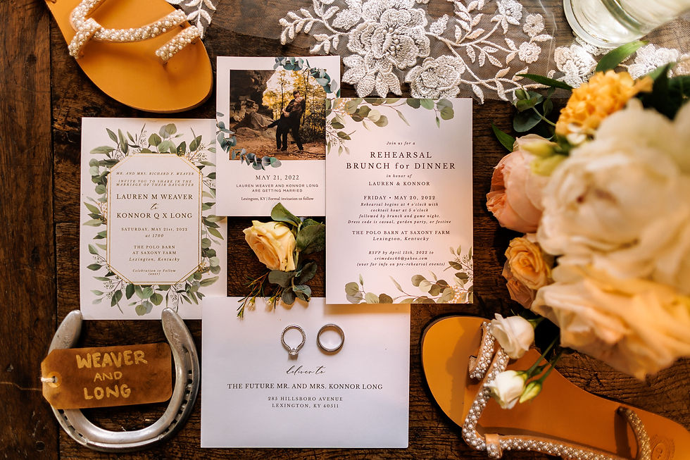 A flat lay of a wedding invitation suite, rings, pearl flip flops, and roses.