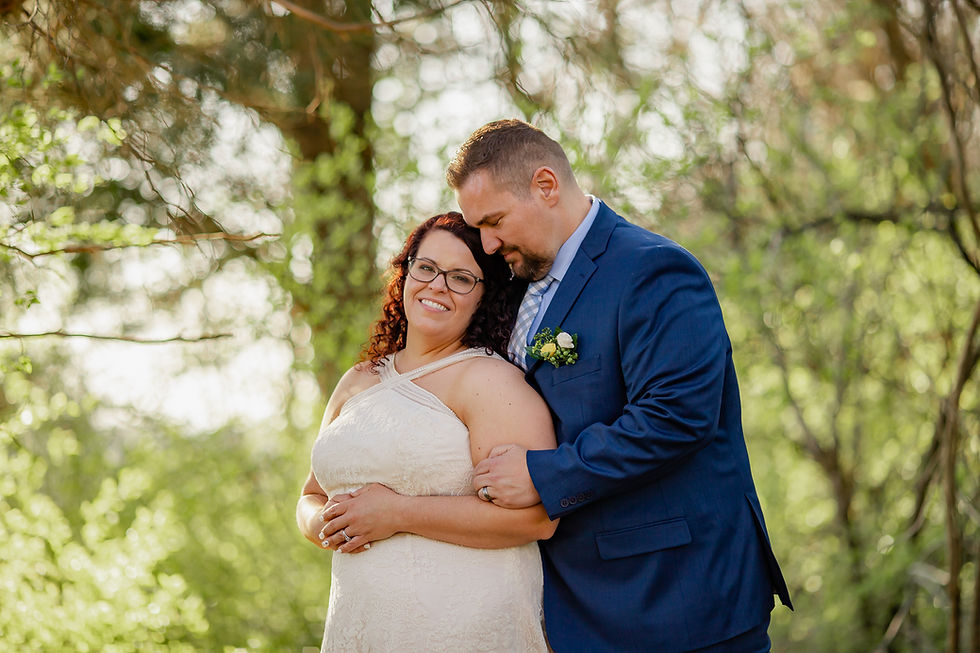 A Wedding couple snuggles up in a cozy pose under trees.