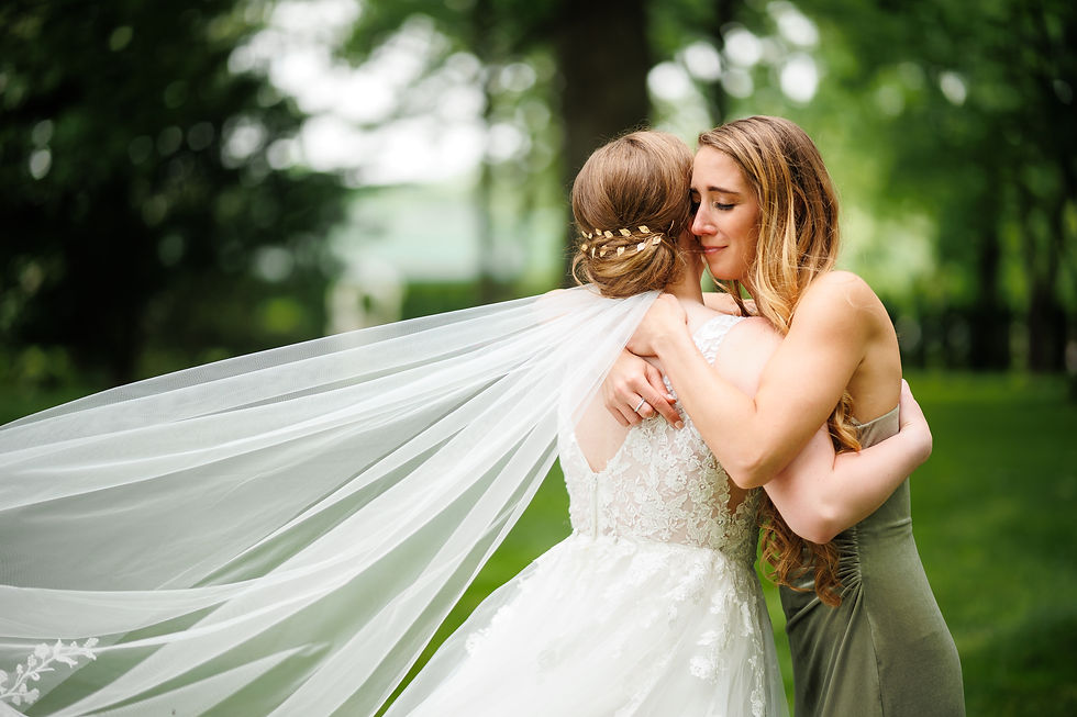 The bride and and bridesmaid hug while the bride's veil flows behind.