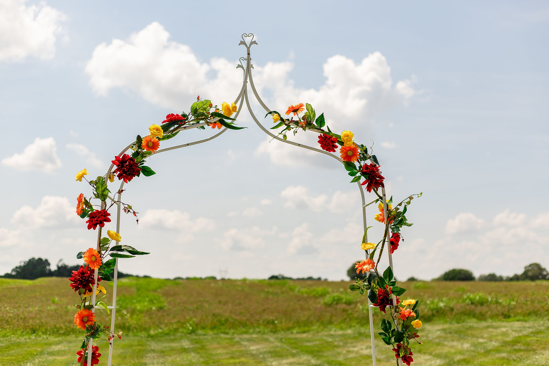 Brightly colored yellow, orange, and red flowers wind around a white metal arch for a wedding alter.