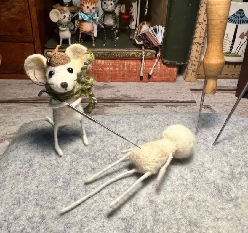 A handmade needle-felted mouse is needle-felting another character.