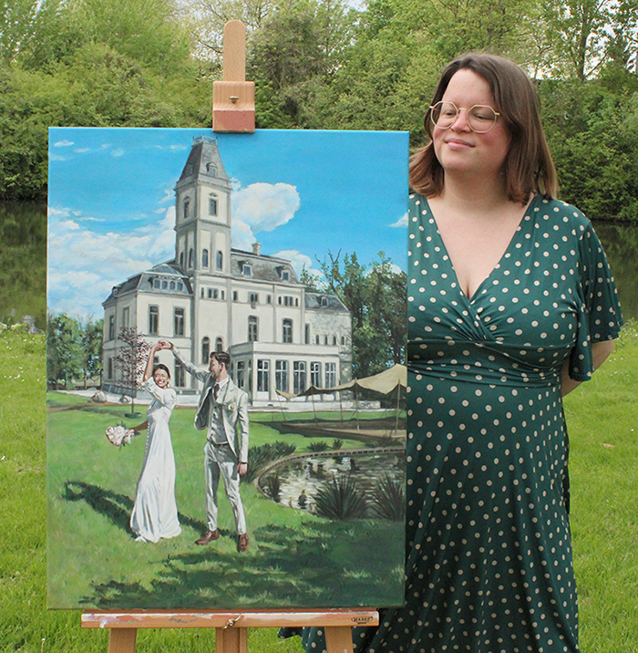 Foto van schilderij op schildersezel in park. Op het schilderij zien we een bruidspaar in danspose in de tuin met op achtergrond een villa. Naast de schildersezel staat RenƩe, Nederlandse vrouw van 32 met donkerblond haar, kijkt tevreden naar doek. Draagt een bril en een groene stippeltjesjurk.
