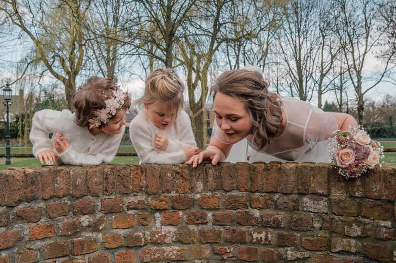Bruid kijkt samen met bruidsmeisjes over een muurtje
