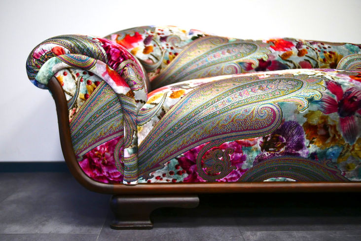 Nahaufnahme eines neu bezogenen Sofas mit detailreichem Paisley-Muster und floralen Akzenten aus der Upperhouse-Kollektion von Saum & Viebahn, kombiniert mit einem geschwungenen Holzgestell.