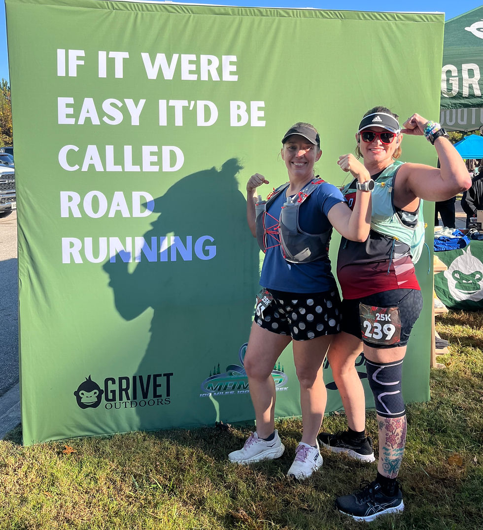 Two smiling female runners flex beside a green sign reading If it were easy it’d be called road running at an outdoor race.
