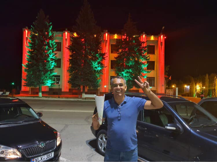 A man stands in a parking lot holding two fingers in a V shape.