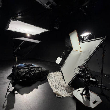 Commercial studio lighting configuration with overhead softboxes and white reflectors surrounding a product staging area in a blacked-out room.