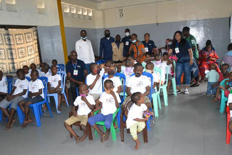 Children wearing Afro Innovation Group t-shirts seated on blue chairs with staff members during a community outreach activity.