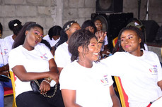Women in white Afro Innovation Group t-shirts sitting together, smiling and laughing during a community workshop.