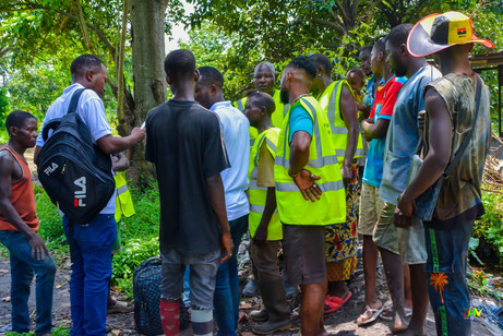Community members and AIG volunteers wearing reflective vests gathered outdoors for an environmental or livelihood activity.