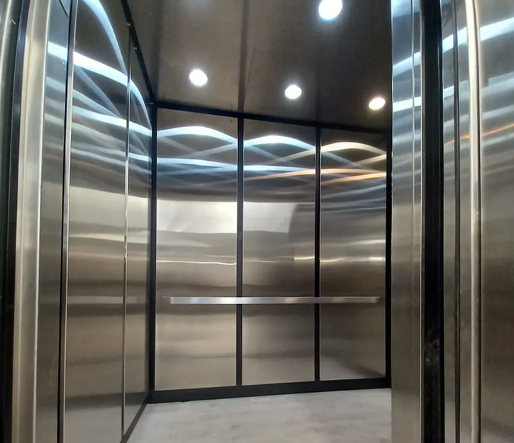 Contemporary stainless steel elevator cab with curved ceiling panels and integrated lighting features