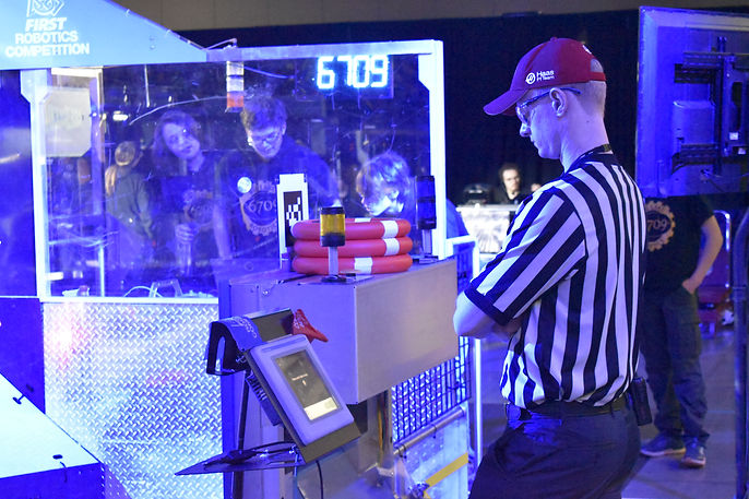Referee standing at his station in blue lighting with our team visible at the driver's sta