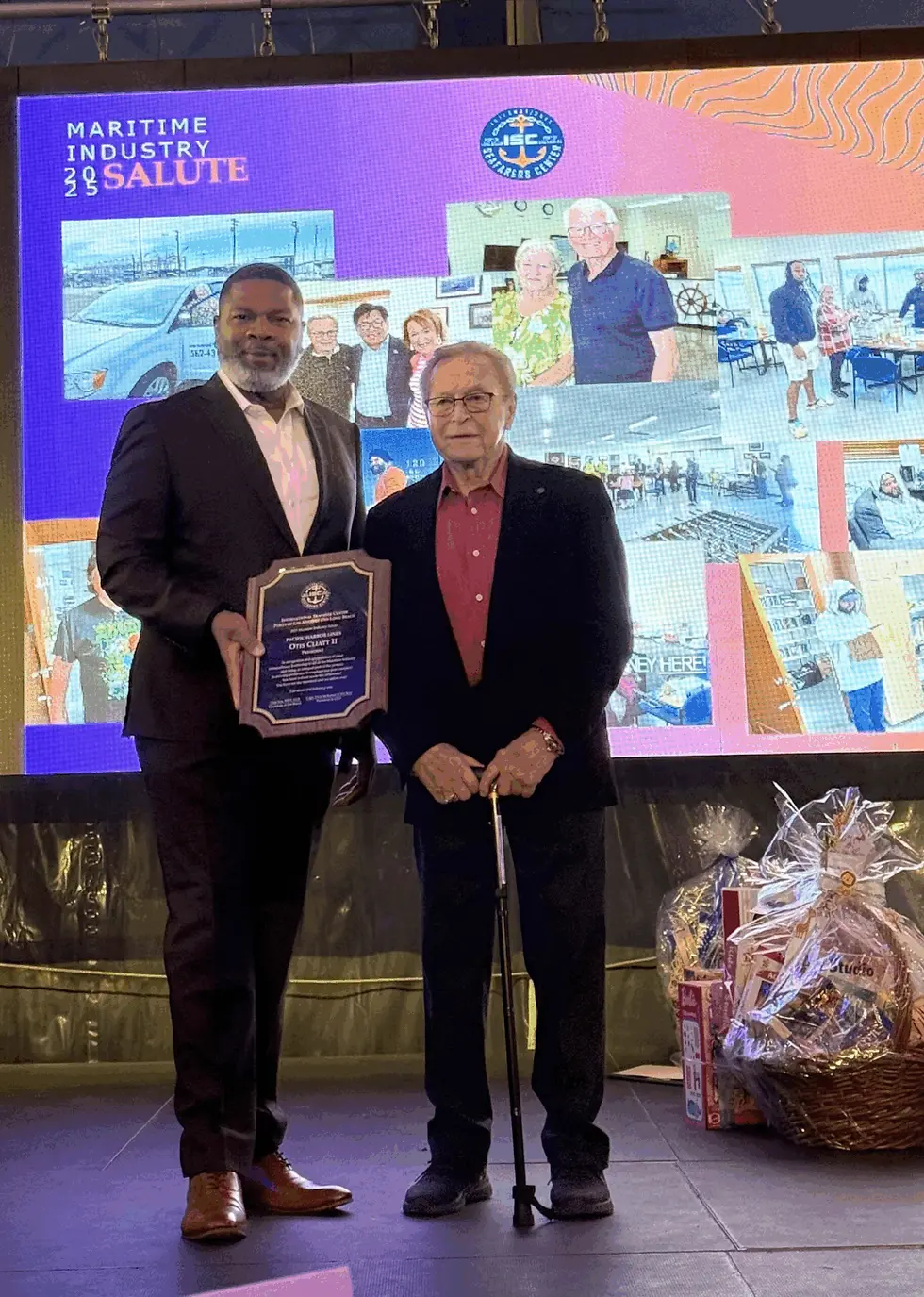 Two men stand on stage, one holding a plaque. The background displays maritime images and "Maritime Industry 2023 Salute" text.