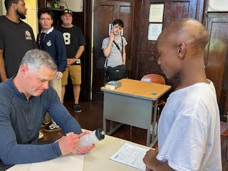 a man at a table signs a clear water bottle while a child in the foreground watches