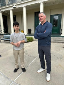 a man in a blue longsleeve shirt and blue pants stands with his arms crossed next to a child