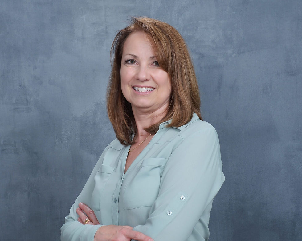 Woman in a light blue blouse smiling with crossed arms against a textured gray background. Mood is confident and friendly.