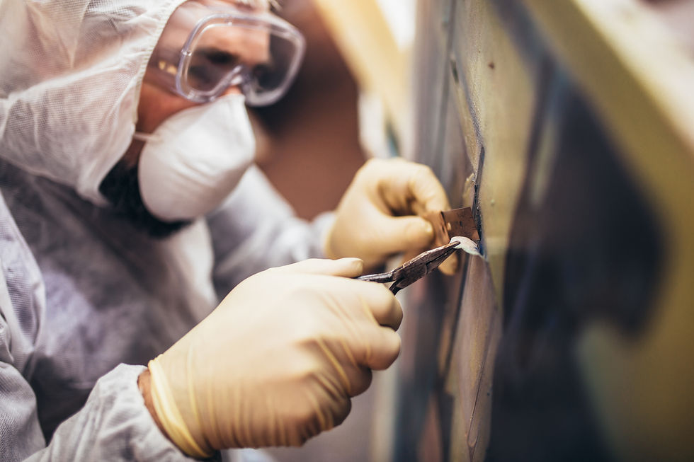 Person in protective suit and goggles carefully scraping a surface with a tool. Focused expression, close-up view, neutral colors.