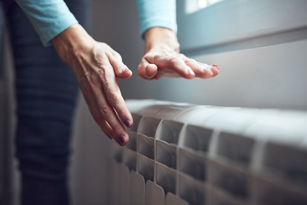 Hands hovering over a white radiator by a window, suggesting a chilly room and a quiet, cozy mood.