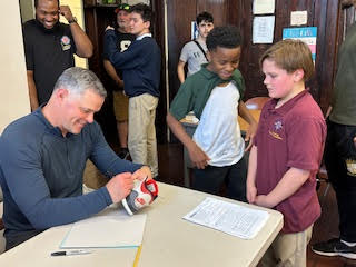 a man at a table signs a clear water bottle while a child in the foreground watches