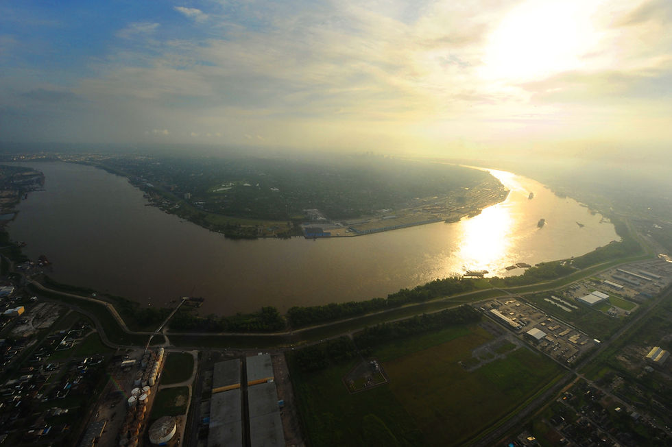 Aerial view of a river bending through lush greenery and urban landscape at sunset. Sunlight reflects on water, creating a serene ambiance.