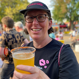 A smiling woman holds a beer in a plastic cup.