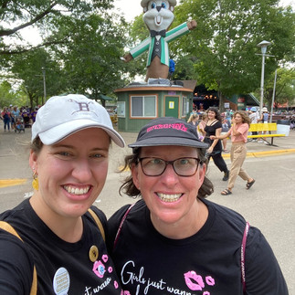 Two women smile in front of a Minnesota State Fair statue.