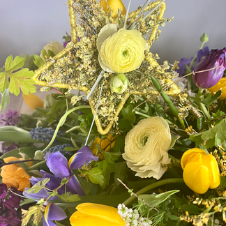 A detail of the hand crafted yellow star placed witihin the colourful casket tribute to celebrate a wonderful life. A Spring floral palette of ruffled ranunculus, elegant tulips and scented stocks. The flowers are designed by Jacqui O of Nantwich, Cheshire