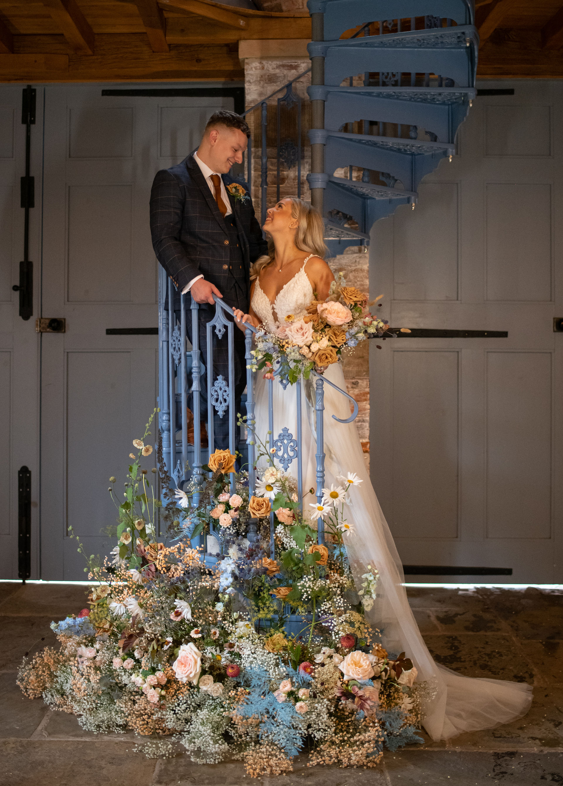 Bride and groom on staircase with caramel eco-dyed baby's breath, toffee roses and man city blue asparagus fern floral installation