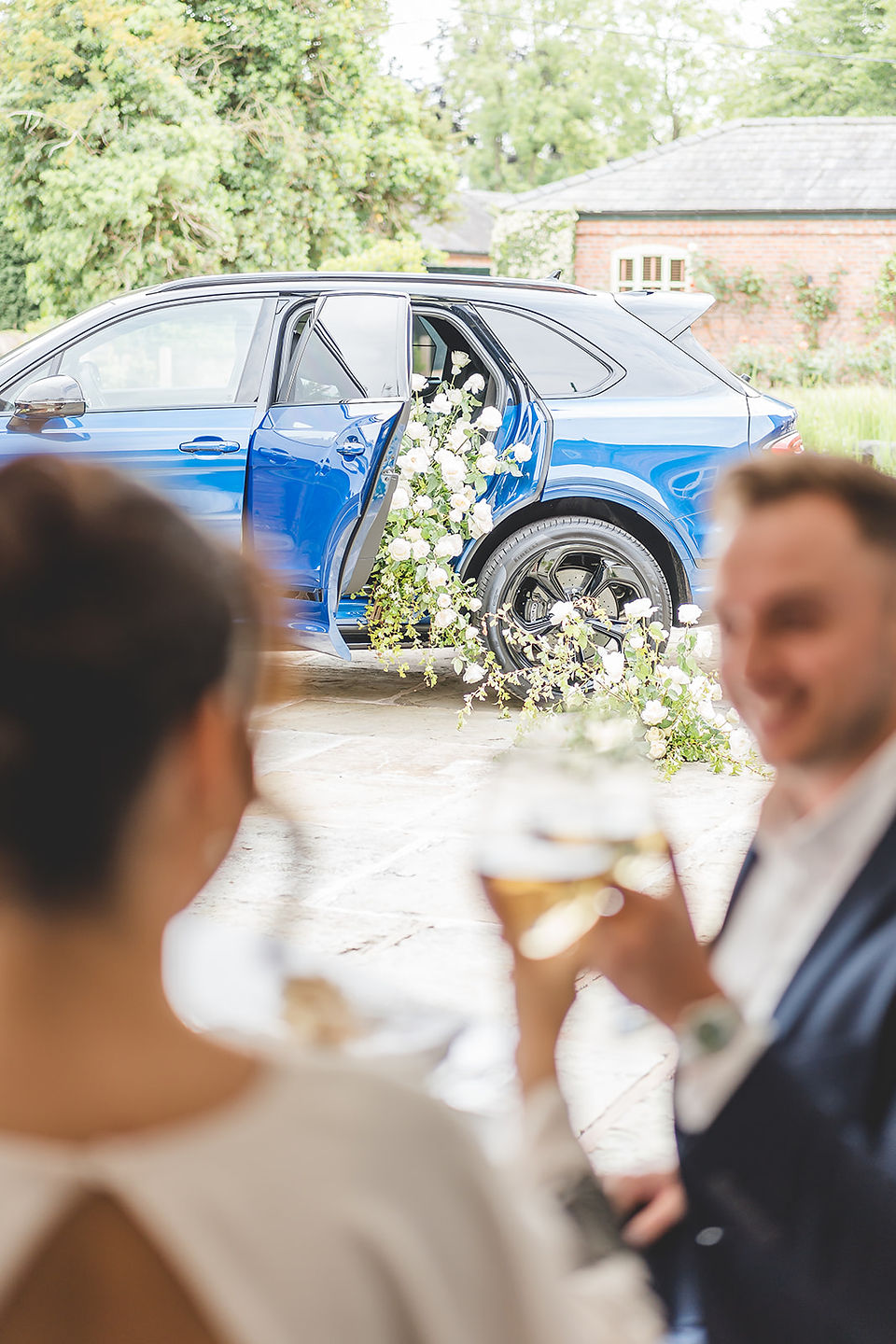 A couple toast to their engagement with a blue bentley in the background