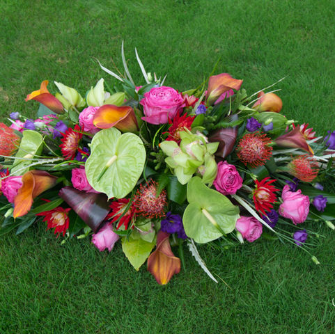A small casket tribute with tropical flowers including anthuriums, calla lilies, and pin heads in vibrant lime, cerise, orange, and purple tones.