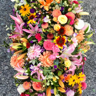 A vibrant sorbet-inspired casket spray in orange, pink, and yellow, featuring fragrant lilies, bold dahlias, and cheerful chrysanthemums arranged to cover the casket in a joyful celebration of life.