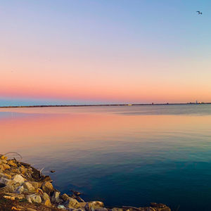 Pastel sunset over calm water with soft pink and blue tones and rocky shoreline