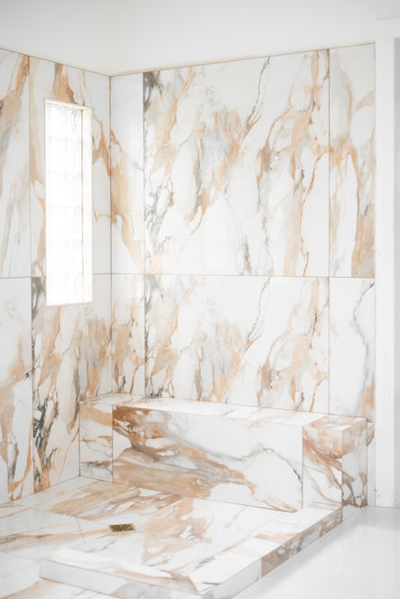Polished white and tan marble tiles with built-in shower bench and floor drain