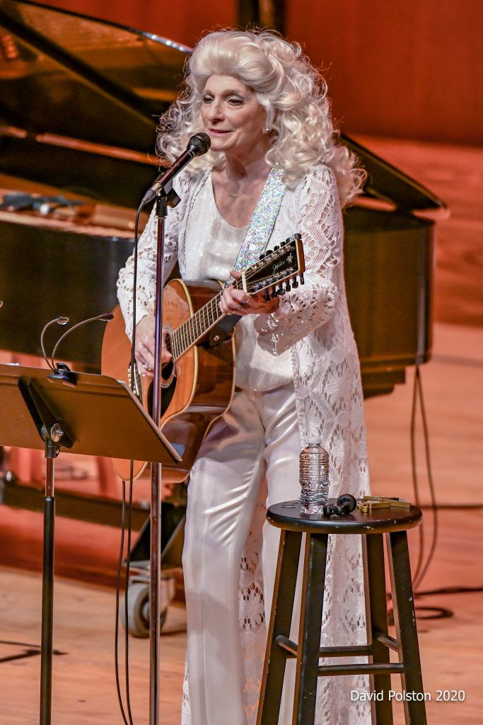 Blonde woman (Judy Collins) playing guitar singing into microphone.