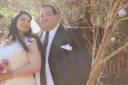 A bride looks lovingly at her husband to her right. Husband look at the camera.