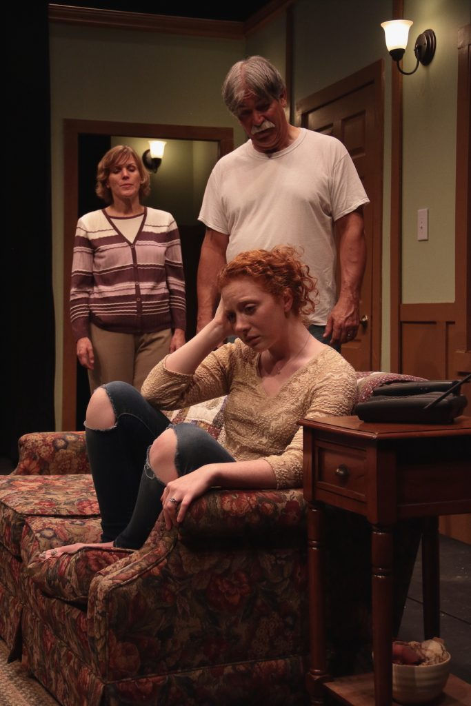 Photo from The Resting Place at the Goode Theater, one actor is distraught on the couch, her mother and father in the background try to console her.