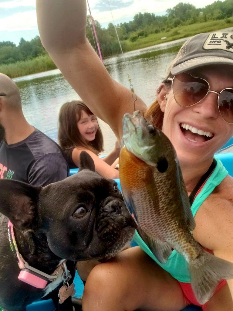 Hailey Neef and family on a boat, they have caught a fish, which their little black dog is sniffing with great interest.