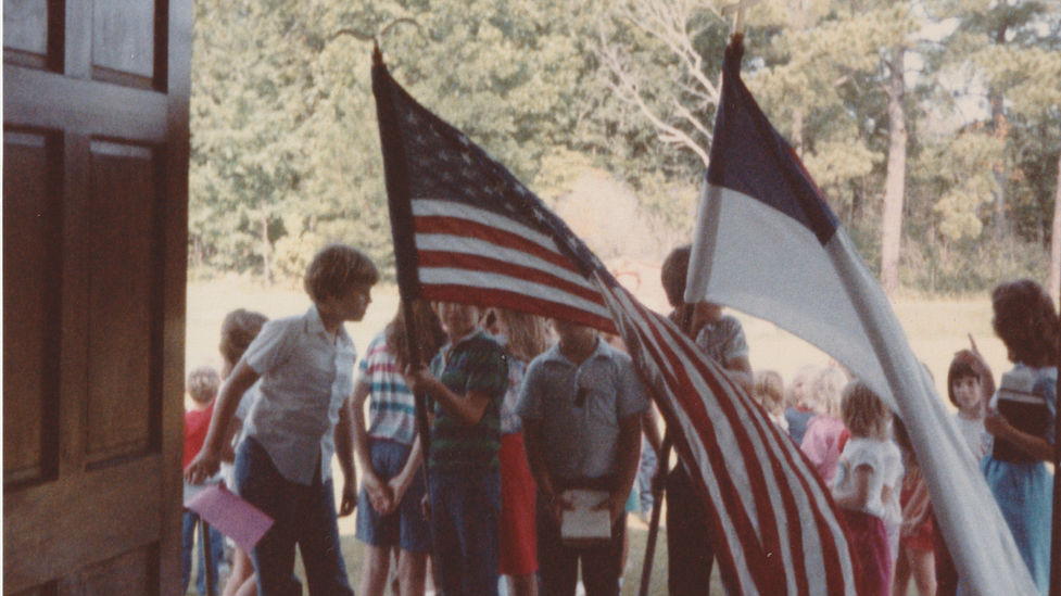 Children holding flags at Life Baptist Church, waving in front of the door.