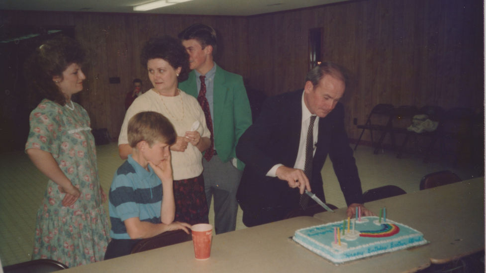 Family cuts cake at a party, with a boy, and the Life Baptist Church.