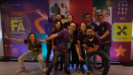 Grupo de pessoas com camiseta rocha, posam em frente ao painel do evento Cliente Fã Festival 2023.