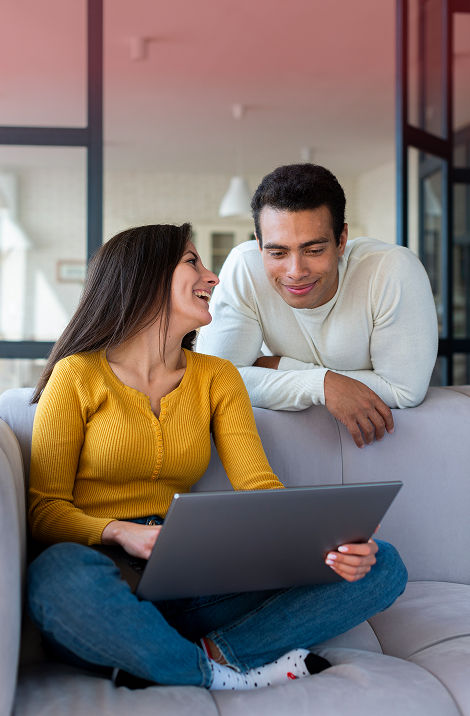 Casal sentado no sofá olhando juntos para a tela de um notebook