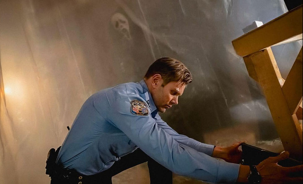 Joel McHale kneeling to fix toolbox as Ghostface watching behind a drop cloth.