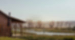Peaceful landscape with a cabin in the foreground and a river with a man fly fishing in the background