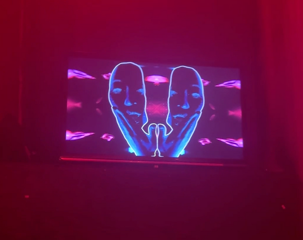 Two mirrored blue digital faces displayed on a screen in a red-lit dark space