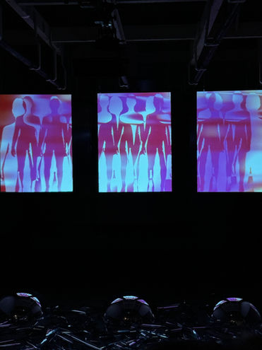 Three screens displaying stylized human figures in blue and purple tones in a dark exhibition space