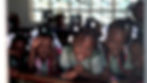 A group of five young Black girls in matching school uniforms leaning on a wooden half wal