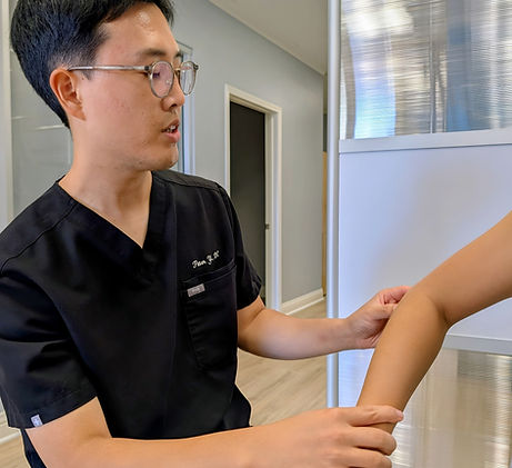 Dr. Peter Yi assessing elbow movement and tenderness for tennis elbow at Reborn Chiropractic in Brea, CA